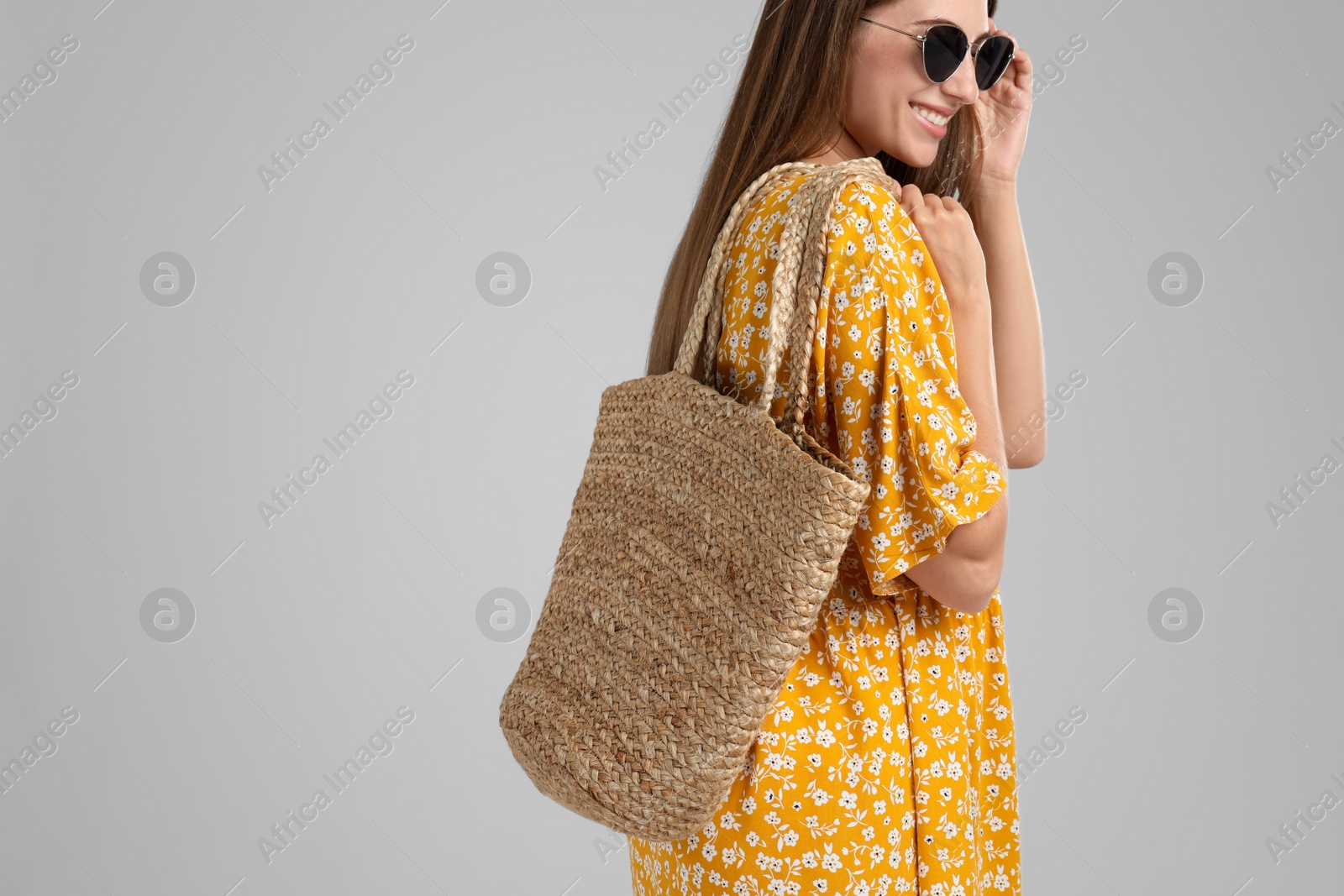 Photo of Beautiful young woman with stylish straw bag on light grey background. Space for text