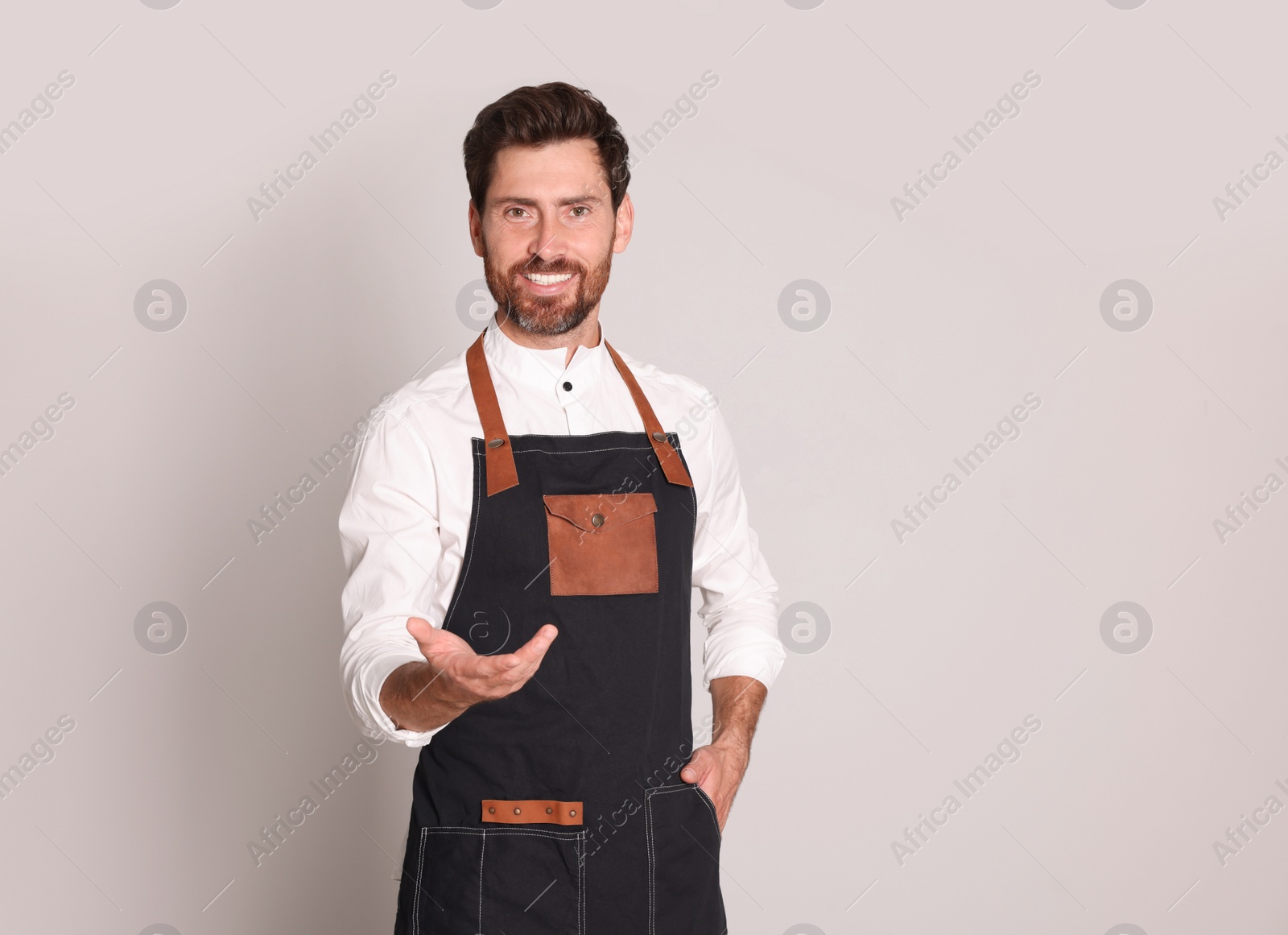 Photo of Smiling hairdresser wearing apron on light grey background, space for text