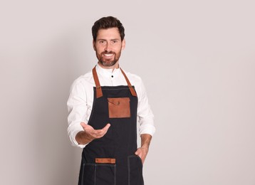 Photo of Smiling hairdresser wearing apron on light grey background, space for text