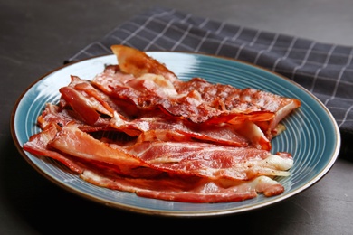 Photo of Slices of tasty fried bacon on dark table, closeup