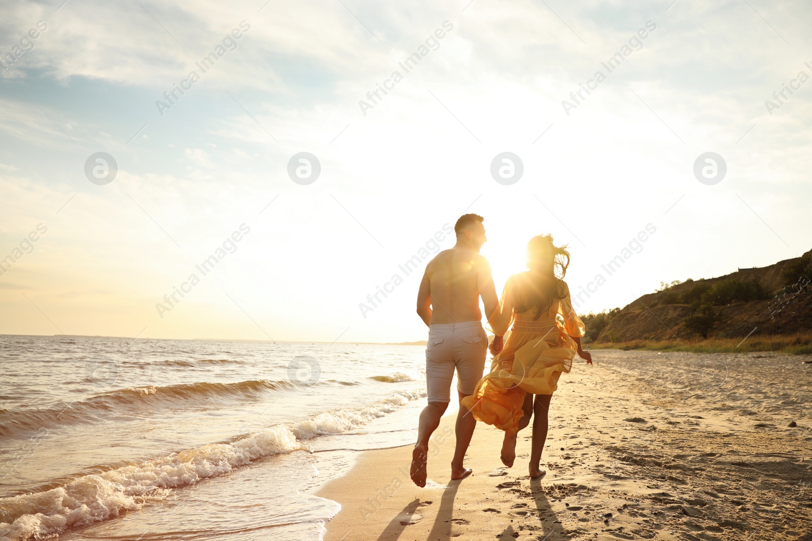 Photo of Lovely couple running together on beach at sunset, back view