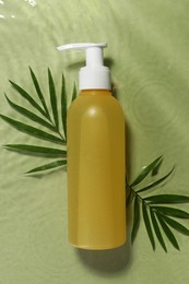 Photo of Bottle of facial cleanser and leaves in water against olive background, flat lay