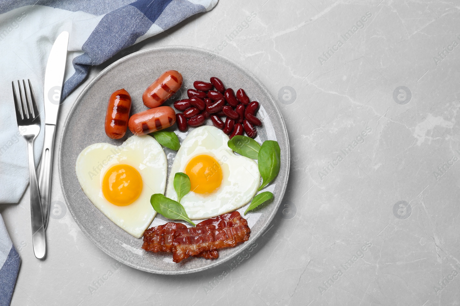 Photo of Tasty breakfast with heart shaped fried eggs served on grey table, flat lay