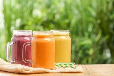 Photo of Different delicious smoothies in mason jars on wooden table against blurred background, space for text