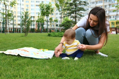 Photo of Young woman with adorable little baby on green grass outdoors. Space for text