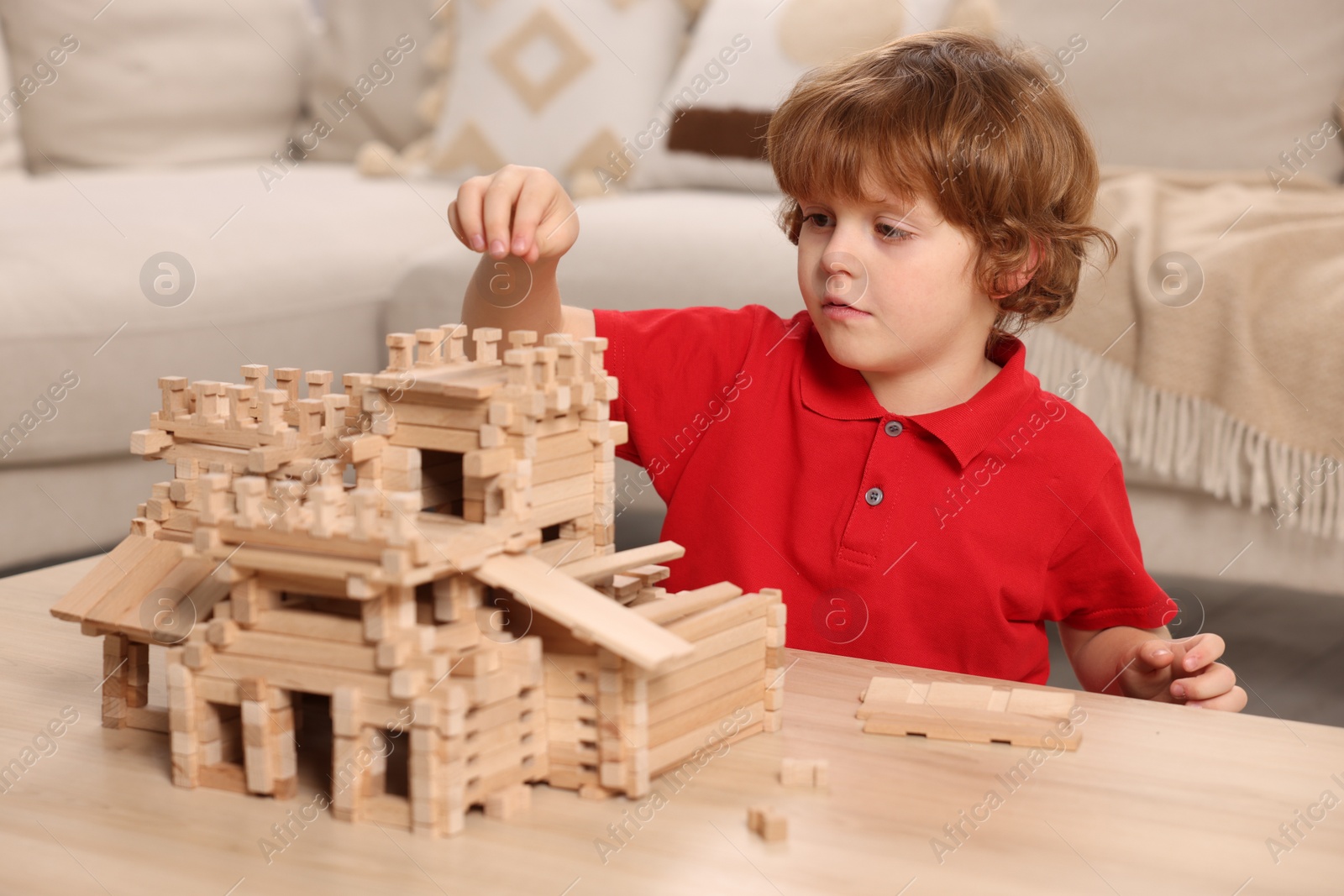 Photo of Cute little boy playing with wooden castle at table in room. Child's toy