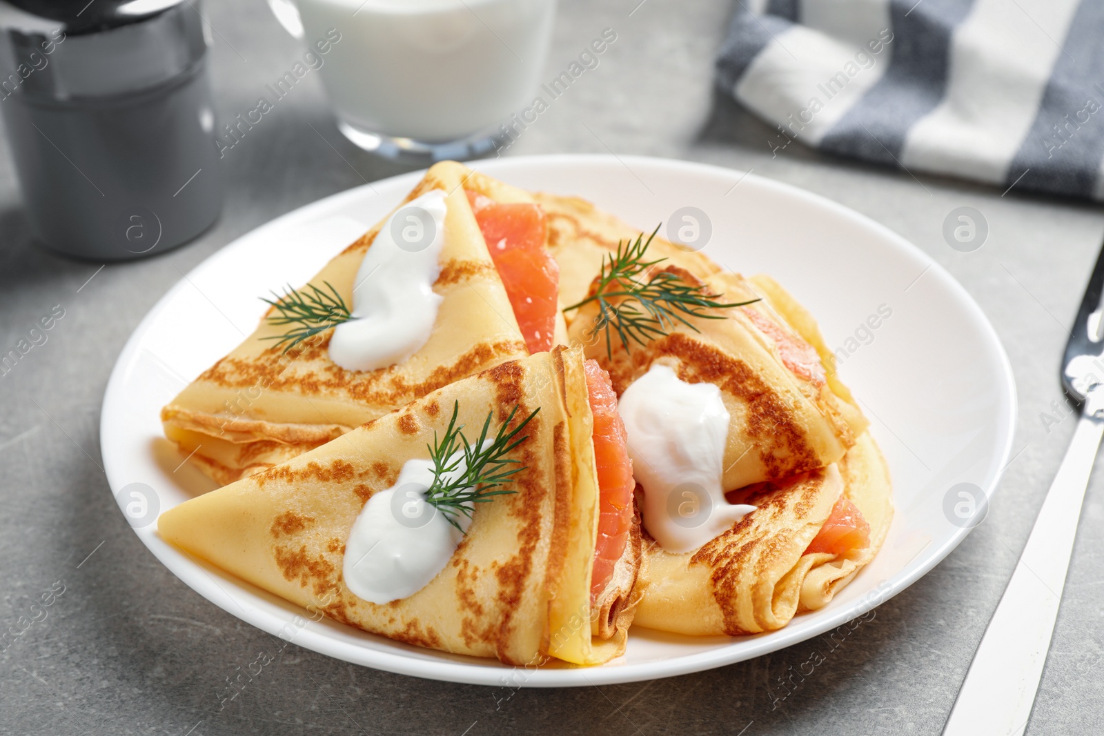 Photo of Delicious thin pancakes with salmon and sour cream on light table