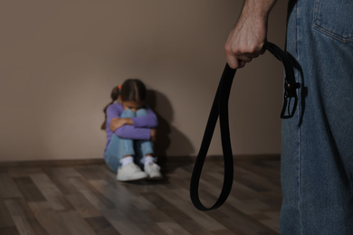 Photo of Man threatening his daughter with belt indoors, closeup. Domestic violence concept
