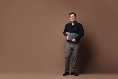 Full length portrait of happy man with laptop on brown background. Space for text