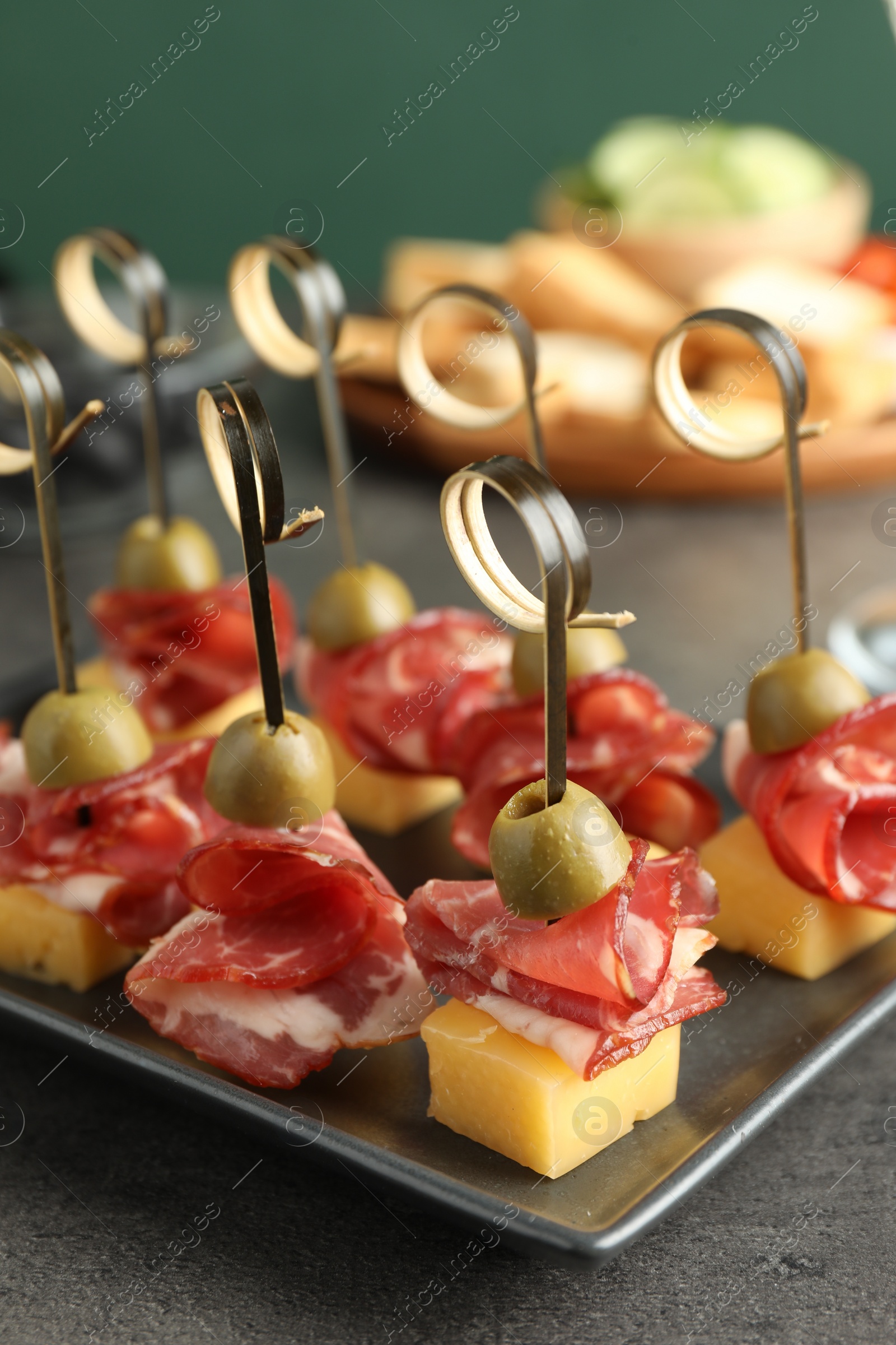 Photo of Tasty canapes with olives, prosciutto and cheese on grey table, closeup