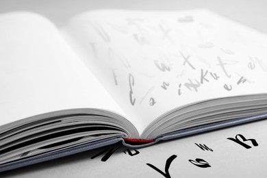 Image of Open book with letters on light grey table, closeup. Dyslexia concept