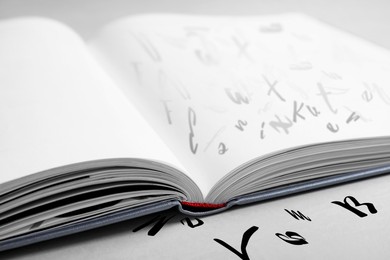 Open book with letters on light grey table, closeup. Dyslexia concept