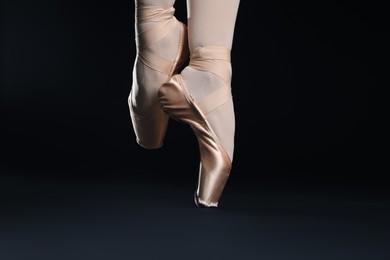 Photo of Ballerina in pointe shoes dancing on black background, closeup