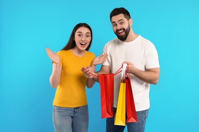 Photo of Excited couple with shopping bags on light blue background