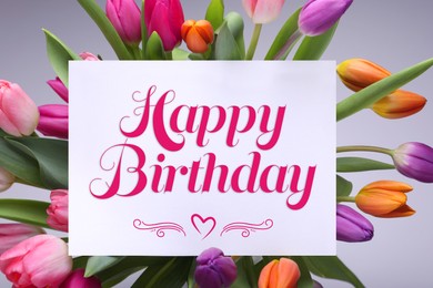 Beautiful bouquet of tulip flowers with Happy Birthday card on light background, top view