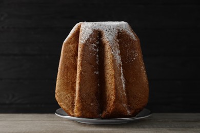 Photo of Delicious Pandoro cake decorated with powdered sugar on wooden table against black background. Traditional Italian pastry