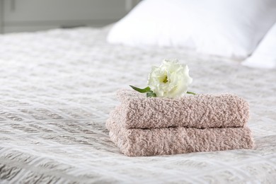 Photo of Stack of clean towels and Eustoma flower on bed, space for text