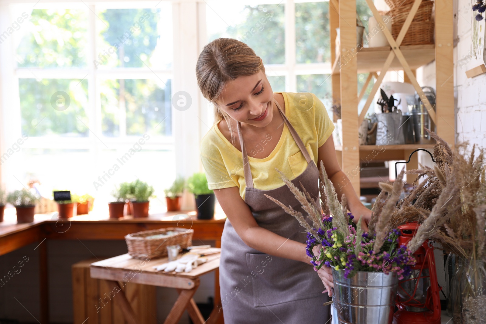 Photo of Young woman taking care of home plants at wooden table in shop