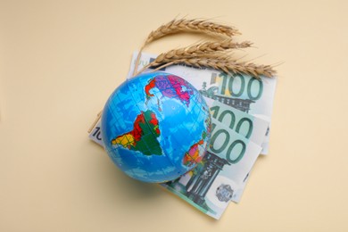 Photo of Import and export concept. Globe, ears of wheat and banknotes on beige background, flat lay