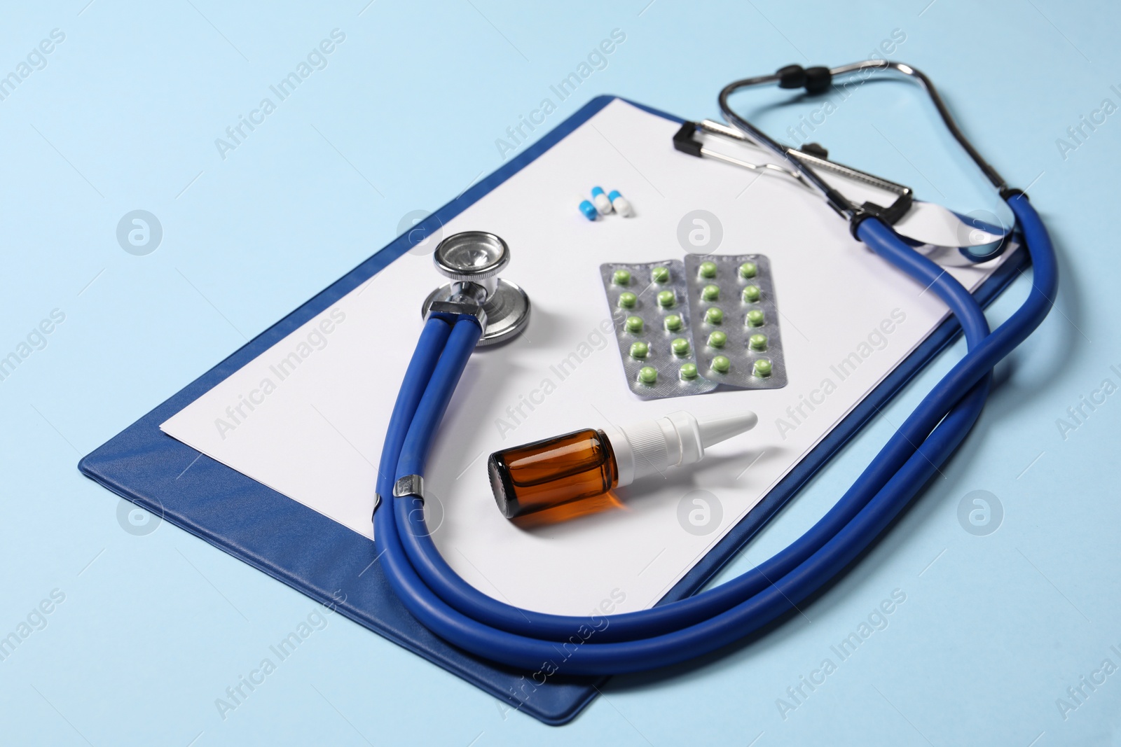 Photo of Stethoscope, pills, nasal spray and clipboard on light blue background, closeup. Medical tool