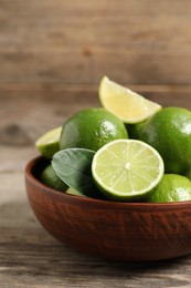 Photo of Tasty ripe limes in bowl on wooden table, closeup