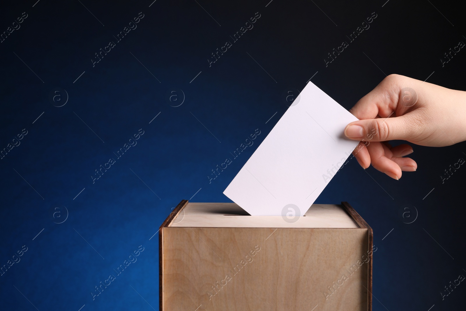 Photo of Woman putting her vote into ballot box on dark blue background, closeup. Space for text