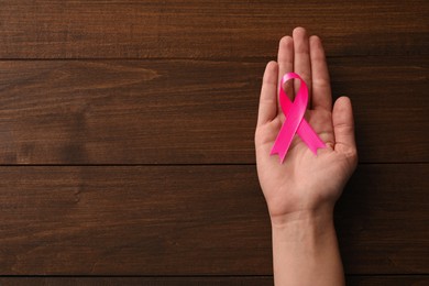 Photo of Woman holding pink ribbon at wooden table, top view with space for text. Breast cancer awareness concept