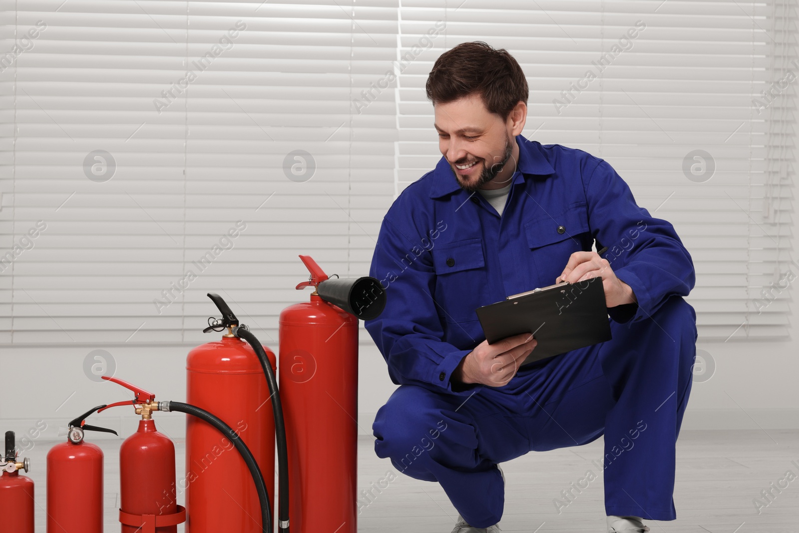 Photo of Man with clipboard checking fire extinguishers indoors