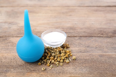 Blue enema, soda powder and dry chamomile flowers on wooden table. Space for text