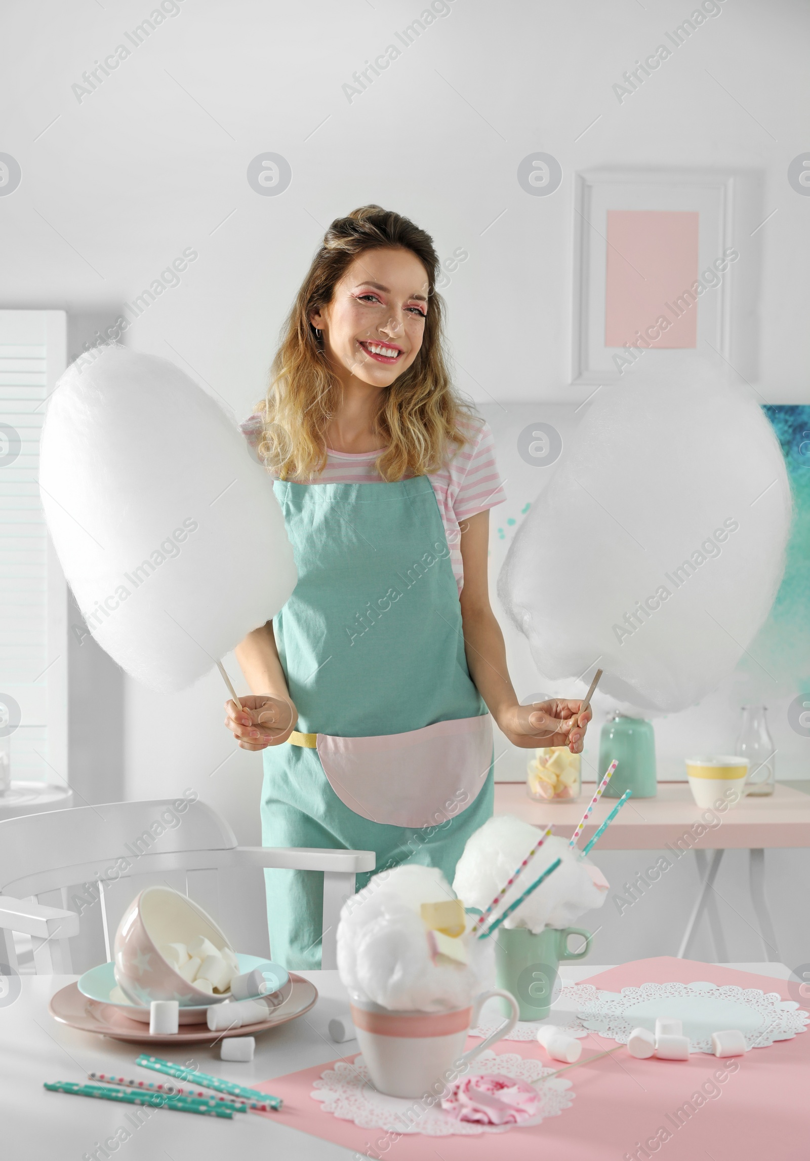 Photo of Happy young woman with cotton candy and sweets on table in room