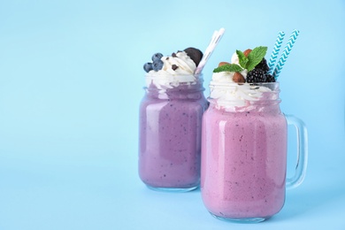 Photo of Tasty milk shakes in mason jars on light blue background. Space for text