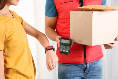 Young woman with smartwatch using terminal for delivery payment indoors, closeup