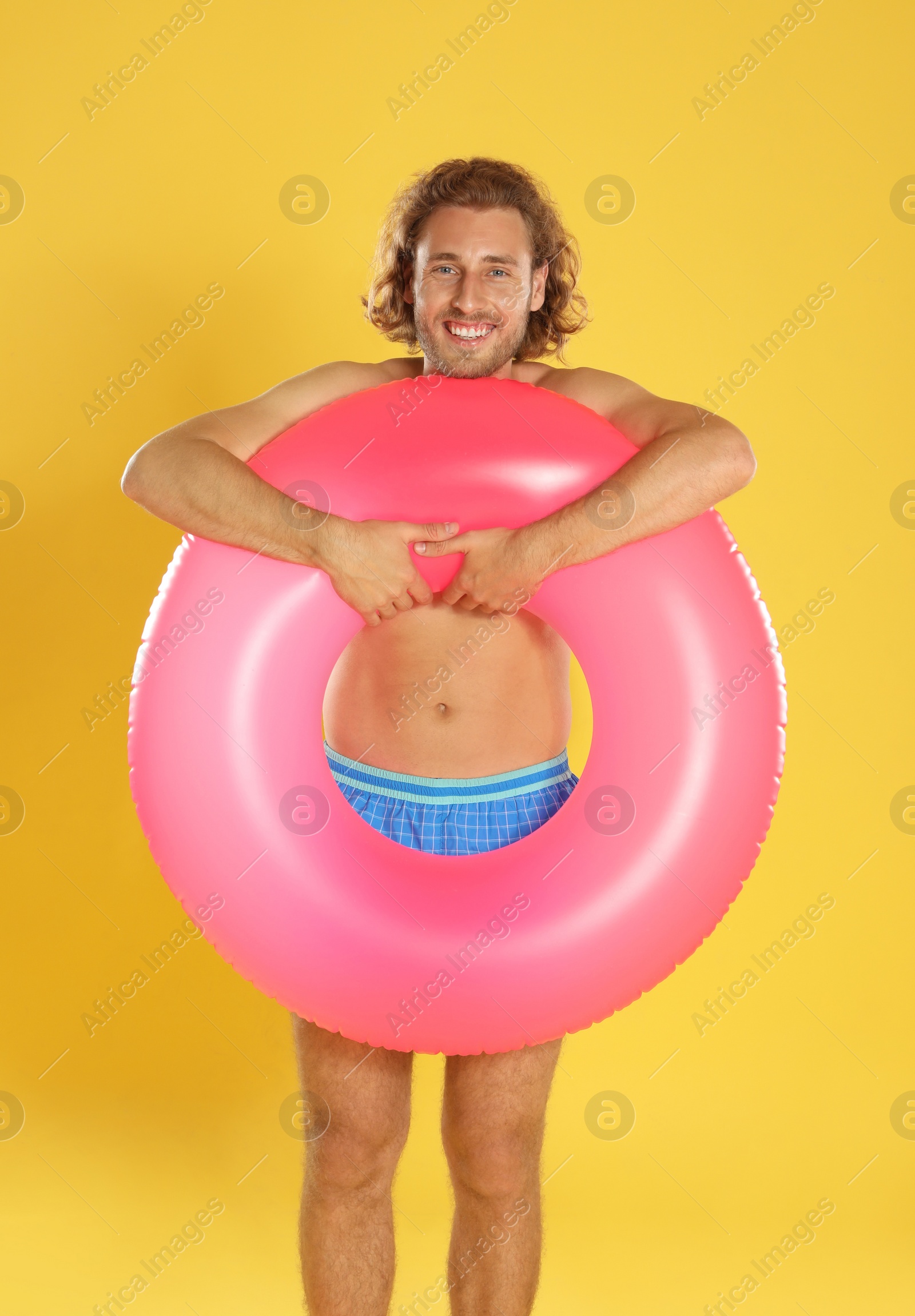 Photo of Attractive young man in beachwear with pink inflatable ring on yellow background