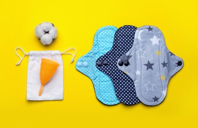 Photo of Reusable cloth pads, menstrual cup and cotton flower on yellow background, flat lay