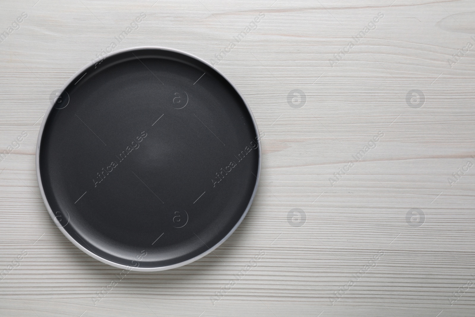 Photo of New dark plate on white wooden table, top view. Space for text