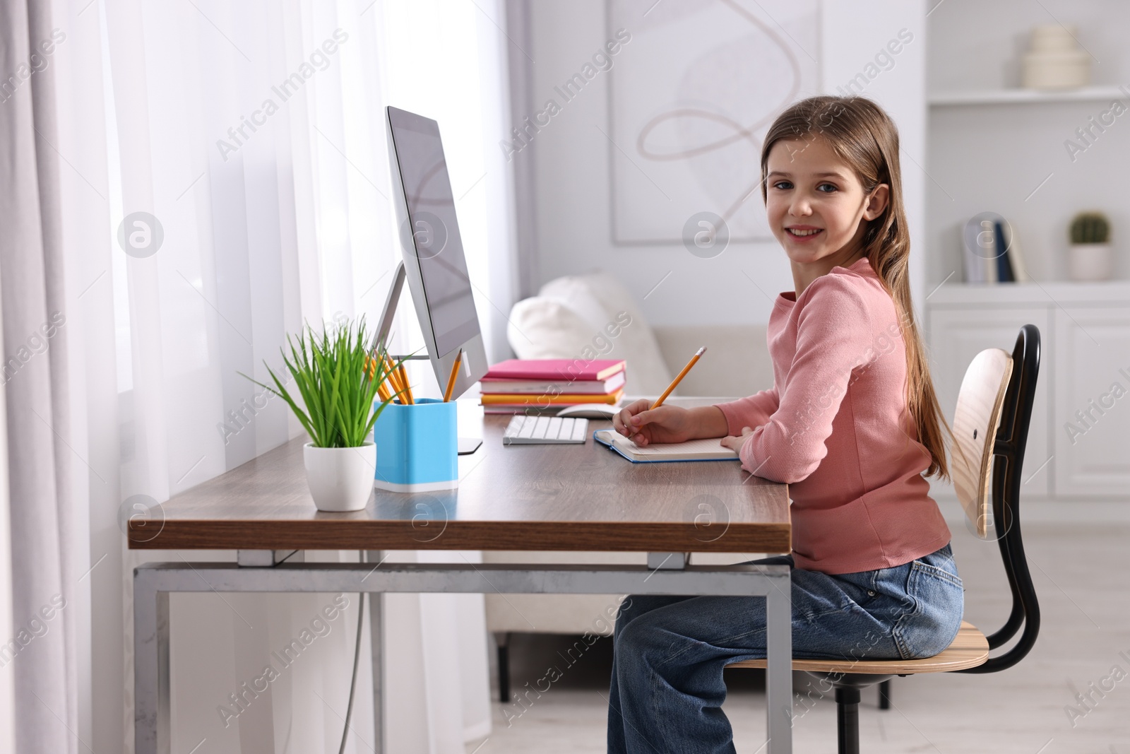 Photo of E-learning. Cute girl taking notes during online lesson at table indoors