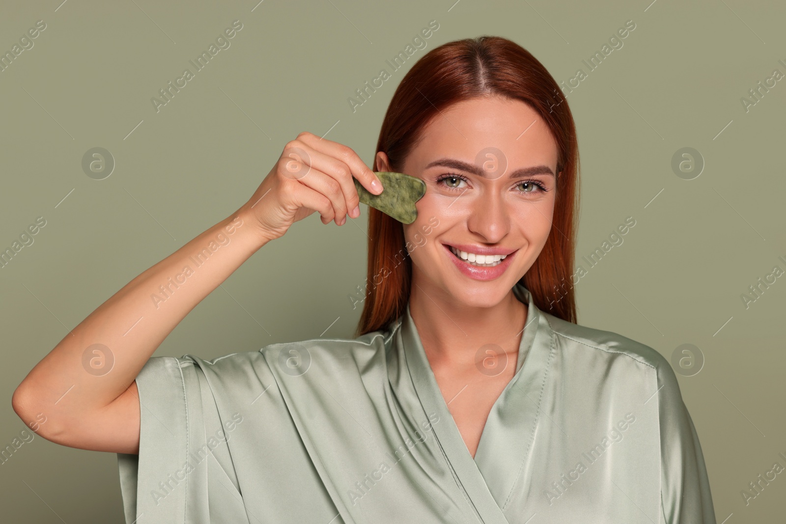 Photo of Young woman massaging her face with jade gua sha tool on green background