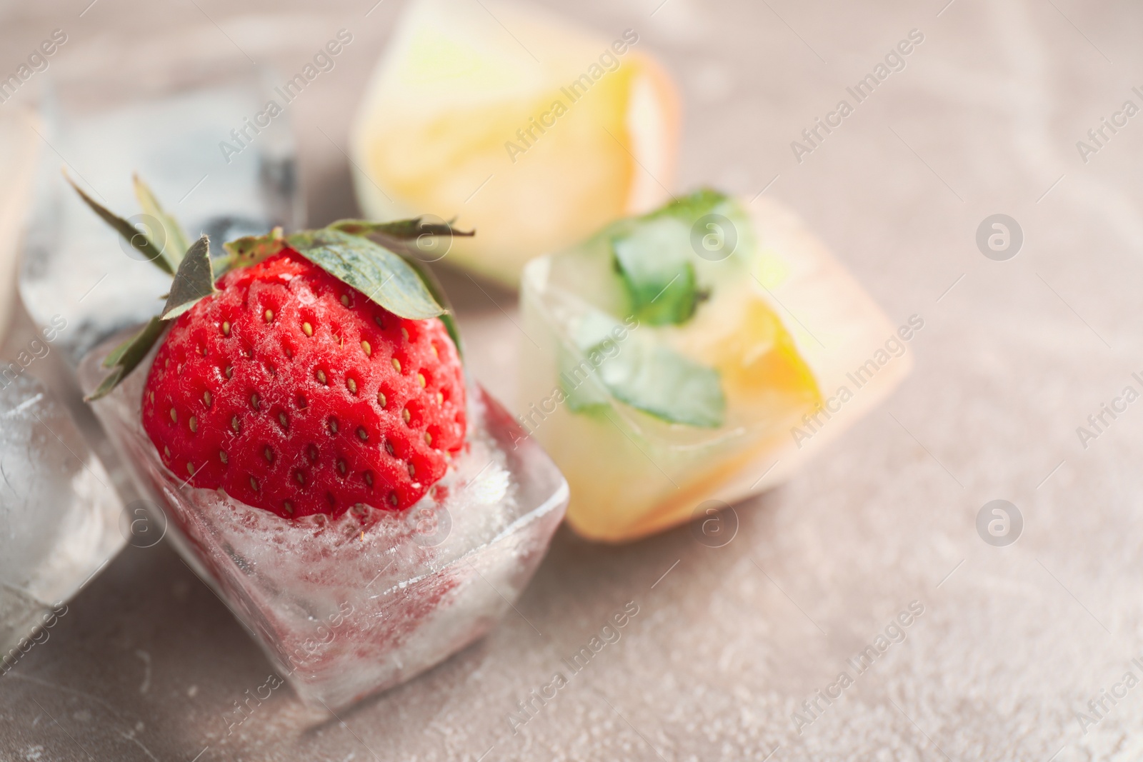 Photo of Ice cubes with different berries and mint on grey table, closeup