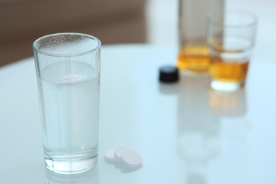 Photo of Glass of hangover remedy and pills on table indoors. Space for text