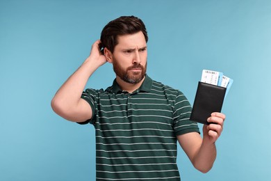 Thoughtful man with passport and tickets on light blue background