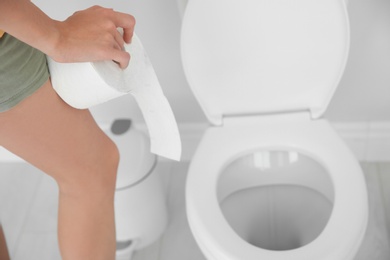 Young woman with bath tissue standing near toilet bowl at home