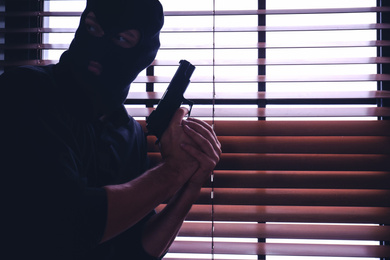 Photo of Man in mask holding gun near window indoors. Space for text
