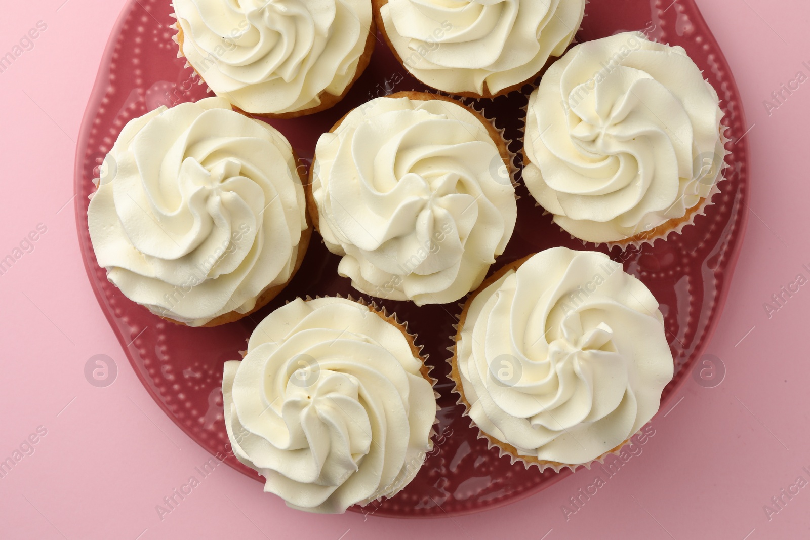 Photo of Tasty vanilla cupcakes with cream on pink background, top view