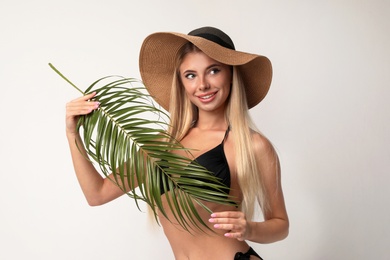 Pretty young woman wearing stylish bikini with palm leaf on light background