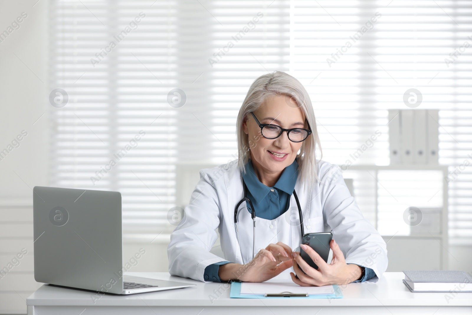 Photo of Mature female doctor with smartphone at table in office