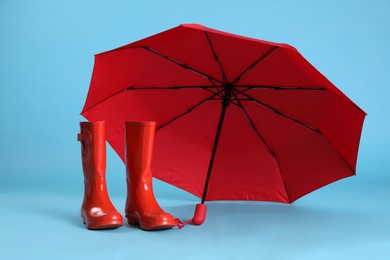 Photo of Open red umbrella and rubber boots on light blue background