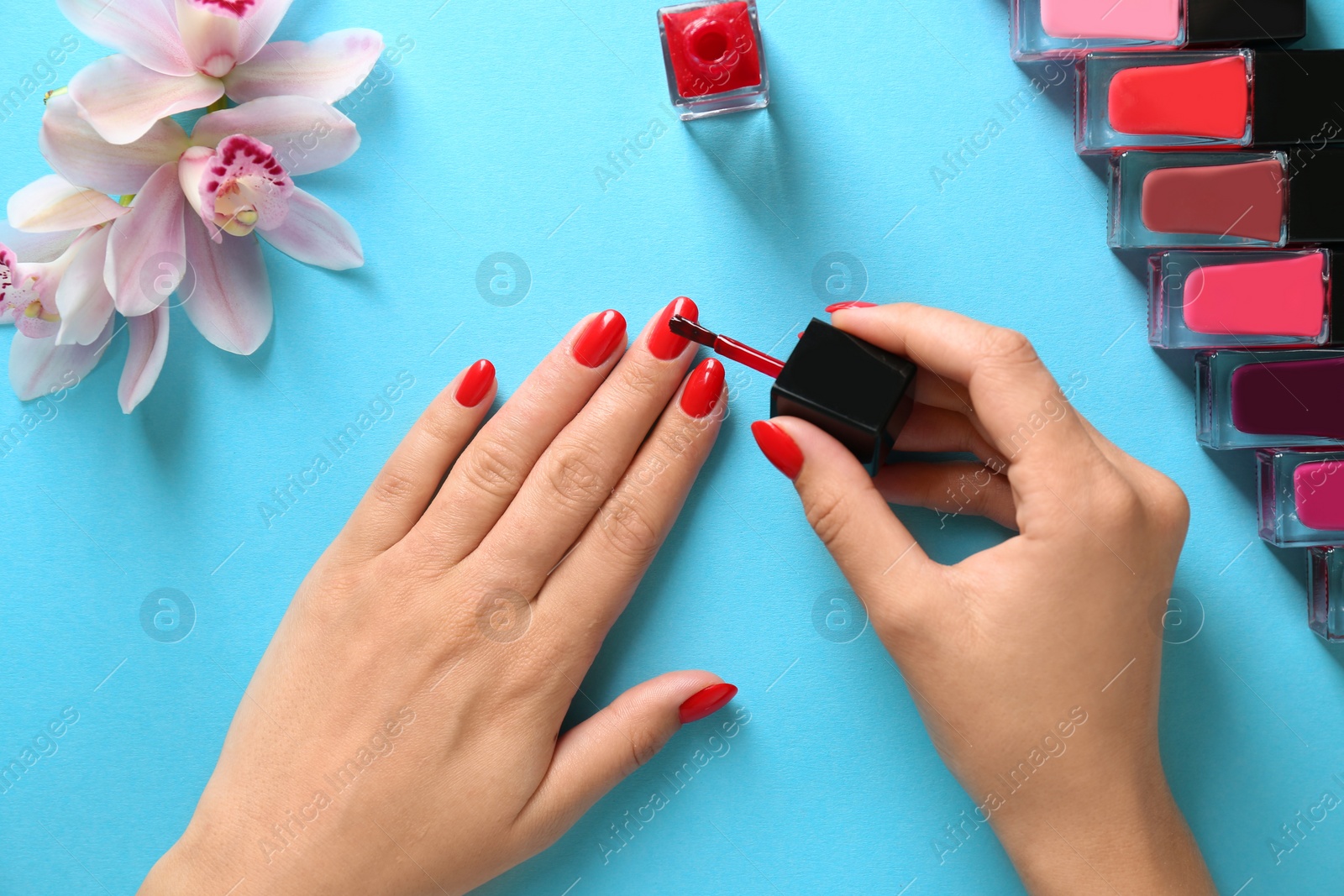 Photo of Woman applying bright nail polish on color background, top view