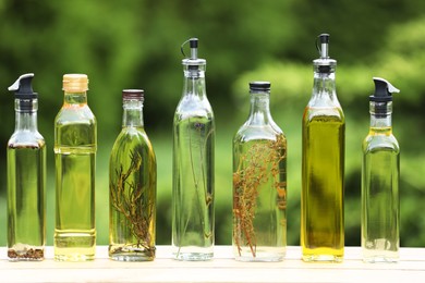 Photo of Many different cooking oils on wooden table against blurred green background