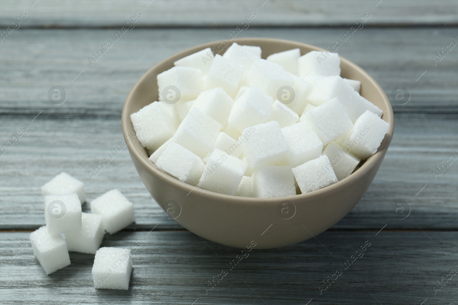 Photo of White sugar cubes in bowl on wooden table, closeup