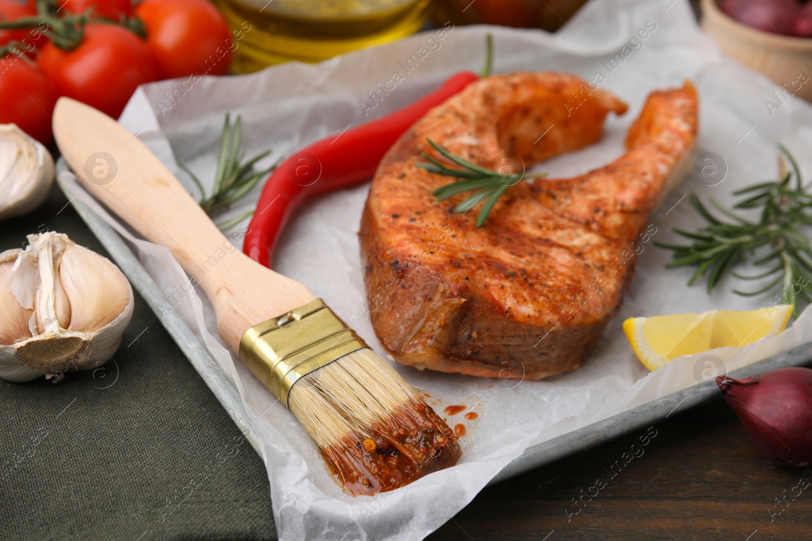 Photo of Fresh marinade, fish, brush and other products on wooden table, closeup